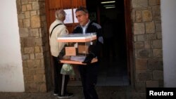 An election worker carries a ballot box while a man looks at the results on the door outside a polling station, a day after the most fragmented national election in Spain's history, in Ronda, southern Spain, Dec. 21, 2015. 