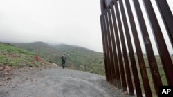 FILE - A Border Patrol agent looks on near where a border wall ends that separates the cities of Tijuana, Mexico, and San Diego, California, Feb. 5, 2019, in San Diego. 