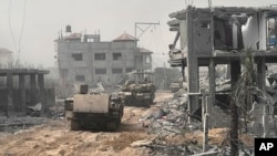 En esta imagen sin fecha distribuida por el ejército israelí, vehículos blindados de transporte de tropas avanzan entre edificios destruidos durante una operación terrestre en la Franja de Gaza.