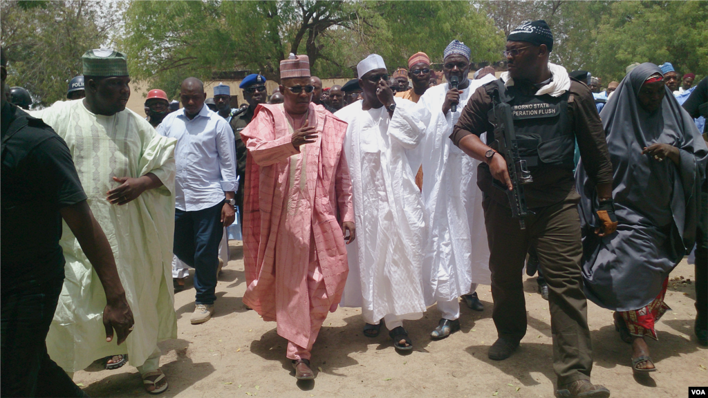 An entourage of Chibok&#39;s governor, the local education commissioner (holding microphone), armed security and townspeople walk toward the site of the burned out government secondary school, Chibok, Nigeria, April 21, 2014. (Anne Look/VOA)