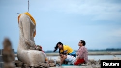 FILE - A family prays near the ruins of a headless Buddha statue, which has resurfaced in a dried-up dam due to drought, in Lopburi, Thailand, Aug. 1, 2019. 