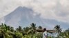 Seorang berjalan di ladangnya saat Gunung Merapi terlihat di latar belakang di Sleman, Indonesia, Kamis, 5 November 2020. (AP Photo/Slamet Riyadi)