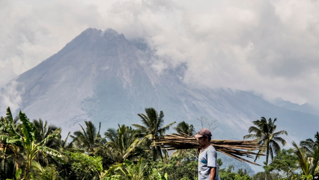 Seorang berjalan di ladangnya saat Gunung Merapi terlihat di latar belakang di Sleman, Indonesia, Kamis, 5 November 2020. (AP Photo/Slamet Riyadi)