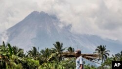 Seorang berjalan di ladangnya saat Gunung Merapi terlihat di latar belakang di Sleman, Indonesia, Kamis, 5 November 2020. (AP Photo/Slamet Riyadi)