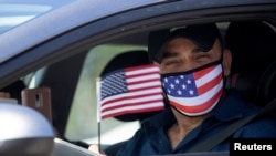 FILE - Palestinian Omar Abdalla waves a US flag after being sworn in as a newly naturalized United States citizens during a drive-through immigration ceremony in an empty parking lot during the COVID-19 outbreak in Santa Ana, Calif., July 19, 2020.