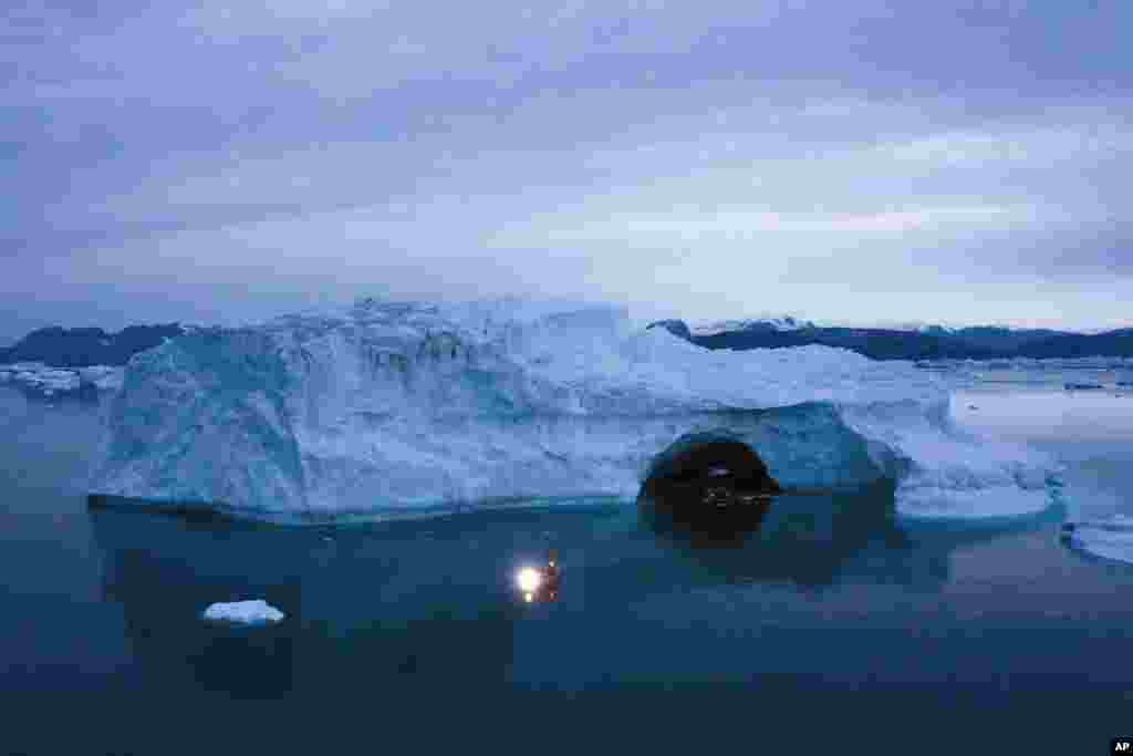 A boat navigates at night next to a large iceberg in eastern Greenland, Aug. 15, 2019. 