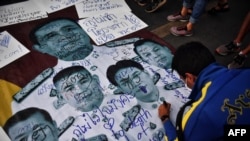 FILE - A protester writes pro-democracy messages on images of Thailand's Prime Minister Prayut Chan-ocha and top Thai generals during an anti-government rally in Bangkok, Feb. 20, 2021.