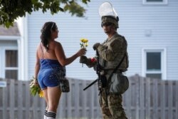FILE - A woman hands flowers to a member of the Wisconsin National Guard standing by as people gather for a vigil, following the police shooting of Jacob Blake, a Black man, in Kenosha, Wis., Aug. 28, 2020.