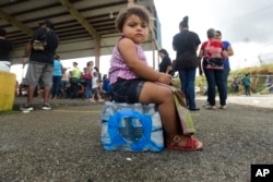 Kerialys Aldea de Jesus sits on bottled water at the Jose de Diego Elementary School where residents file FEMA forms for federal aid in the aftermath of Hurricane Maria in Las Piedras, Puerto Rico, Oct. 2, 2017.