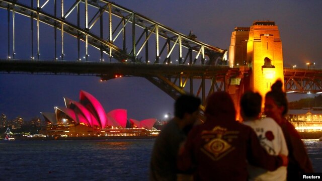 A group of people sit on a stone wall in front of the Sydney Opera House as it is illuminated in pink lights to mark the marriage equality bill being passed this week by the Australian parliament in Sydney, Australia, Dec. 8, 2017. 