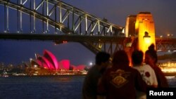 Sekelompok orang duduk di depan Gedung Opera Sydney yang diterangi lampu pink untuk menandai undang-undang pernikahan sesama jenis yang ditandatangani minggu ini di Sydney, Australia, 8 Desember 2017. 