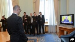 PM Ukraina Arseniy Yatsenyuk (depan kiri) menyaksikan pidato presiden terguling Ukraina Viktor Yanukovych dari Rostov-on-Don, sebuah kota di Rusia, yang ditayangkan dalam acara berita di televisi di Kyiv, Ukraina (28/2).