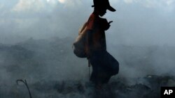 Smoke from burning trash fires swirls around a Cambodian boy as he scavenges a dump on the outskirts of Phnom Penh, file photo. 