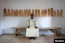 FILE - Aboubakar Yaro, head of conservation at the Djenne Library of Manuscipts, sits next to Koranic scripts written on pieces of wood in Djenne, Mali, Sept. 1, 2012.