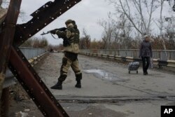 FILE - A Russia-backed rebel stands guard on a newly reconstructed bridge which connects rebel-controlled territory and government-controlled territory in Stanytsia Luhanska, eastern Ukraine, Oct. 27, 2015.