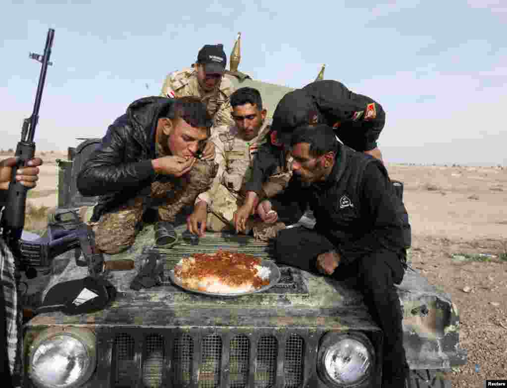 Beberapa tentara Irak dan pejuang Syiah makan di atas kendaraan militer di Baiji, utara Baghdad.