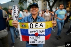 A demonstrator holds up a Venezuelan national flag with a message that reads in Spanish; "OAS, don't leave us alone in this fight," in Caracas, Venezuela, June 21, 2017.