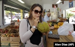 FILE - Lillian Nguyen of New York sips coconut water at a fruit store in the Little Havana area of Miami, June 9, 2015.