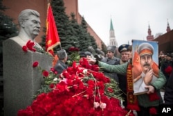 A woman holding a portrait of Josef Stalin places flowers near the monument signifying his grave near the Kremlin wall, marking the anniversary of Stalin's birth, in Moscow's Red Square, Dec. 21, 2017.