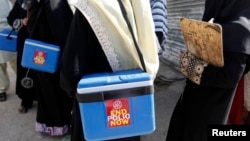 FILE - Polio vaccinators carry boxes of vaccine drops as they head toward sites where they will administer them in Karachi, Pakistan, Oct. 21, 2014.