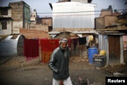 FILE - A man walks past a temporary shelter built near houses which were damaged during the earthquakes last year, in Bhaktapur, Nepal.