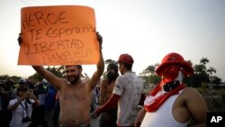 A protester holds a sign that reads in Spanish "Hero. We're waiting for you. Freedom. Let's go Venezuela" at the bridge where guardsmen are blocking the entry of U.S.-supplied aid, in La Parada, Colombia, Feb. 25, 2019, on the border with Venezuela. 