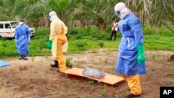 In this photo taken on Friday, June 19, 2015, the wrapped remains of a new born child suspected of contracting the Ebola virus, lays on a stretcher as health workers, dressed in Ebola protective gear, move the body for burial in Dubreka, Guinea. Despite hopes that the deadly Ebola outbreak could soon be contained in West Africa, it shows no signs of abating in Guinea and may be flaring up once more in Sierra Leone as people are flouting rules limiting travel meant to stop it. (AP Photo/Youssouf Bah)