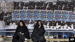 Iranian women sit at bus stop, in front of parliamentary elections campaign posters in the city of Qom, 78 miles (125 kilometers) south of the capital Tehran, March 1, 2012.