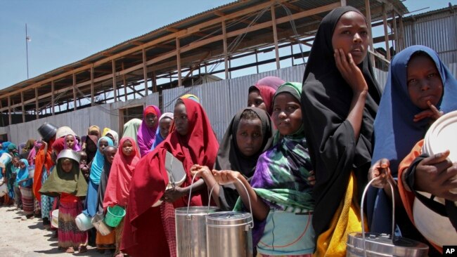 FILE - Displaced Somali girls who fled the drought in southern Somalia stand in a queue to receive food handouts at a distribution center in a camp in Mogadishu, Somalia, Feb. 25, 2017.