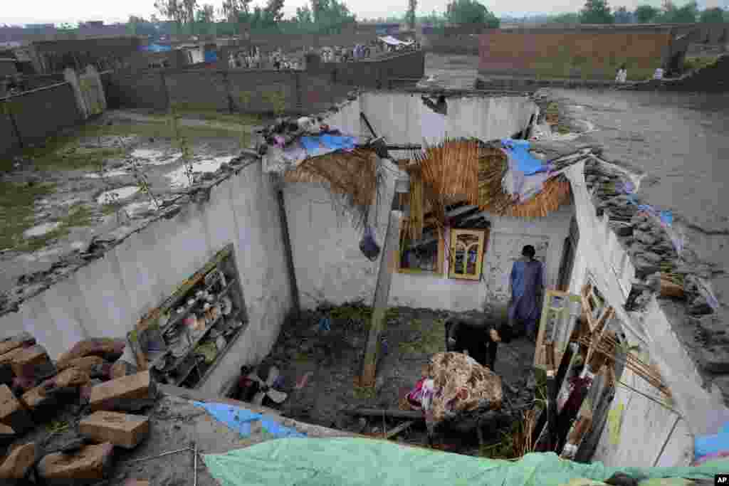 Orang-orang mengumpulkan barang milik mereka dari sebuah rumah yang rusak berat akibat hujan deras dan badai angin Minggu malam (26/4) di Peshawar, Pakistan.