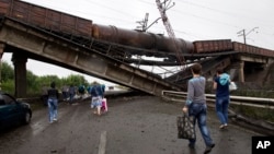 People walk under a destroyed railroad bridge over a main road leading into Donetsk, near the village of Novobakhmutivka, north of Donetsk, eastern Ukraine, July 7, 2014.