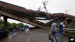 Warga berjalan di bawah jembatan kereta api yang runtuh ke jalan utama menuju Donetsk, Ukraina timur (7/7). 