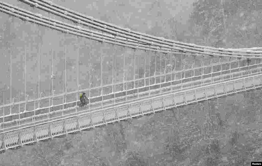 A person cycles over the Clifton Suspension Bridge and Avon Gorge in Bristol during snowfall in southwest Britain, Feb. 1, 2019. 