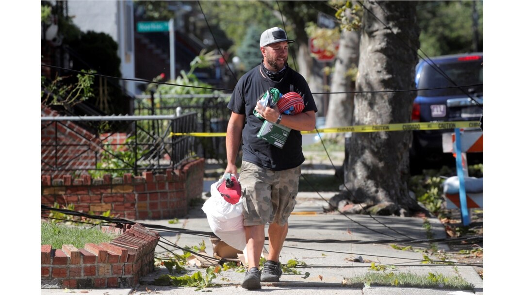 A man carries supplies as he walks over fallen tree limbs and downed power lines in the aftermath of Tropical Storm Isaias in the Sheepshead Bay Area of Brooklyn, New York, Aug. 4, 2020.