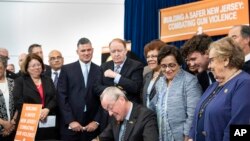 In this photo provided by the New Jersey Governor's Office, Gov. Phil Murphy, center, signs several gun safety bills at the Richard J. Hughes Justice Complex Atrium in Trenton, N.J., June 13 , 2018. 