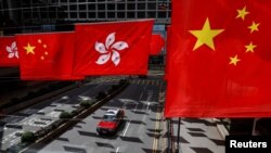 一辆出租车行驶在香港街道，一旁的购物中心外悬挂了香港旗帜和中国国旗。（路透社，2023年7月5日）