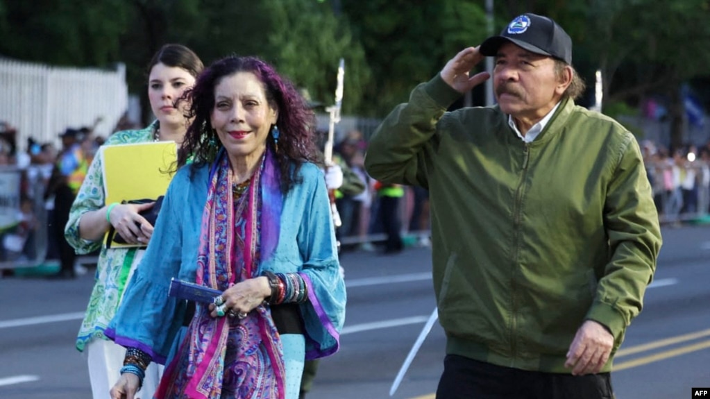 ARCHIVO - Daniel Ortega, acompañado por su esposa y vicepresidenta, Rosario Murillo, saludando a su llegada a un desfile militar para conmemorar el 44º aniversario de la revolución nicaragüense. 