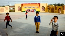 Ujgurska djeca igraju se na trgu na kojem je plakat koji prikazuje Han Kineze i Ujgure kako zajedno poziraju na fotografiji s natpisom "Trg jedinstva novog sela u gradu Hotan", u novom selu Unity u Hotanu u zapadnoj kineskoj regiji Xinjiang, septembra. 20. 2018.