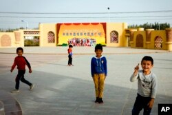 FILE - Anak-anak Uyghur bermain di alun-alun dengan latar belakang poster propaganda bergambar warga Tionghoa Han dan Uighur bertuliskan "Alun-Alun Persatuan Desa Baru Persatuan Kota Hotan", di wilayah Xinjiang, China barat, 20 September 2018. (AP/Andy Wong, File)