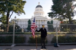 Christian Alvarado holds a U.S. flag in front of a fence surrounding the California Capitol in Sacramento, Jan. 16, 2021. The fence was built because of concerns that protests around Joe Biden's inauguration as president Jan. 20 could turn violent.