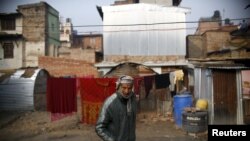 FILE - A man walks past a temporary shelter built near houses which were damaged during the earthquakes last year, in Bhaktapur, Nepal.