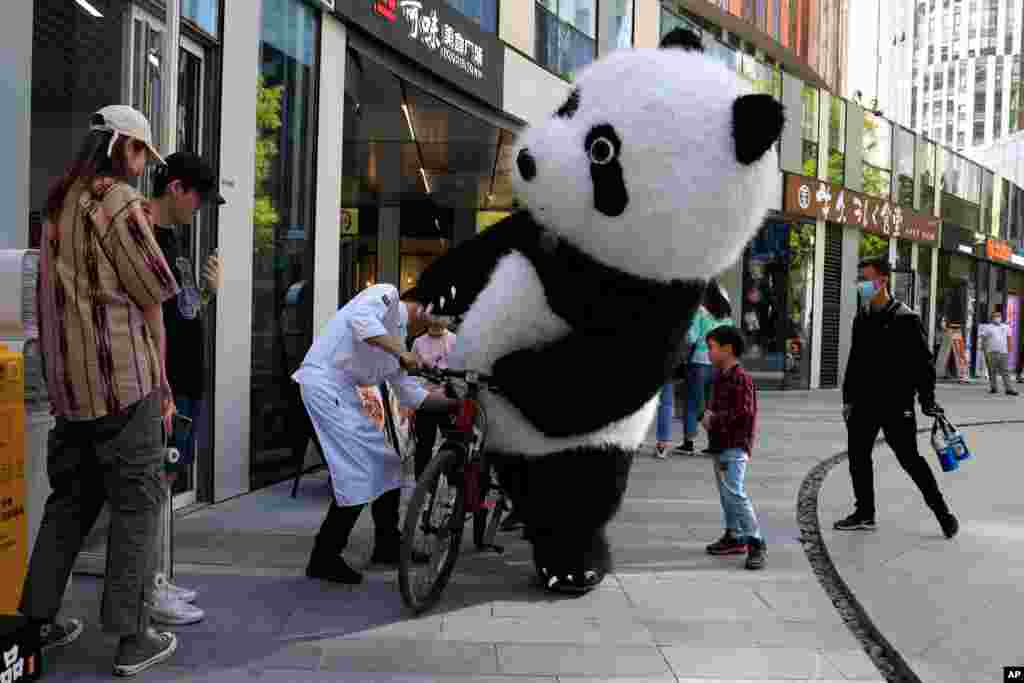 A panda mascot tries to ride a bicycle with the aid of a chef in Beijing, China.