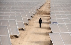 FILE - A man walks through panels at a solar power plant in Aksu, Xinjiang Uyghur Autonomous Region, April 5, 2012.