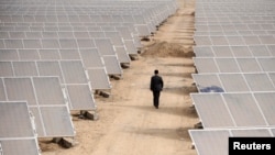 FILE - A man walks through panels at a solar power plant in Aksu, Xinjiang Uyghur Autonomous Region, April 5, 2012. 