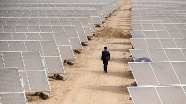 FILE - A man walks through panels at a solar power plant in Aksu, Xinjiang Uyghur Autonomous Region, April 5, 2012.