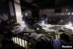 People search through papers as they join members of the Syrian civil defense group, known as the White Helmets, to search for prisoners underground at Sednaya prison, in Sednaya, Dec. 9, 2024.