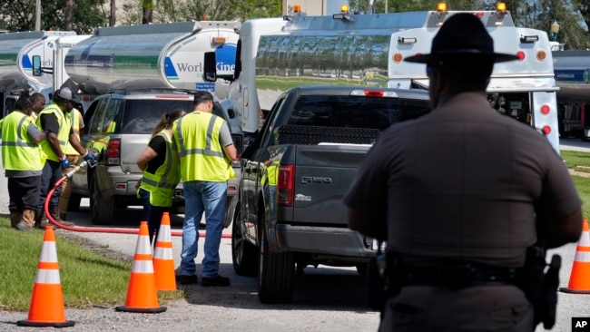 A Florida Highway Patrol officer watches as fuel depot workers distribute gas to residents, Oct. 12, 2024, in Plant City.