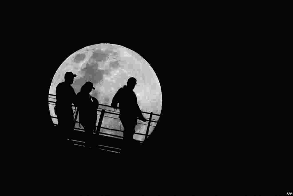 Tiga warga tampak siluetnya dengan latar belakang bulan purnama saat mereka turun dari puncak Jembatan Pelabuhan Sydney, Australia. (AFP)&nbsp;