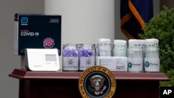 FILE - Materials for COVD-19 testing from Abbott Laboratories, U.S. Cotton, and Puritan are displayed as President Donald Trump speaks about the coronavirus during a press briefing in the Rose Garden of the White House, May 11, 2020, in Washington.