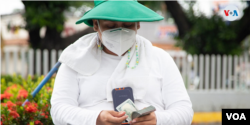 Personas dedicadas al cambio de dólares, conocidos como "cambistas", se cubren la cara para protegerse del coronavirus en las calles de Managua, Nicaragua. Agosoto de 2021. [Fotografía: Houston Castillo Vado]